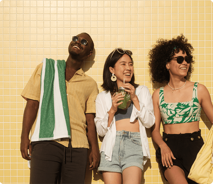 Young man and two young women, happily leaning against a yellow-tiled wall